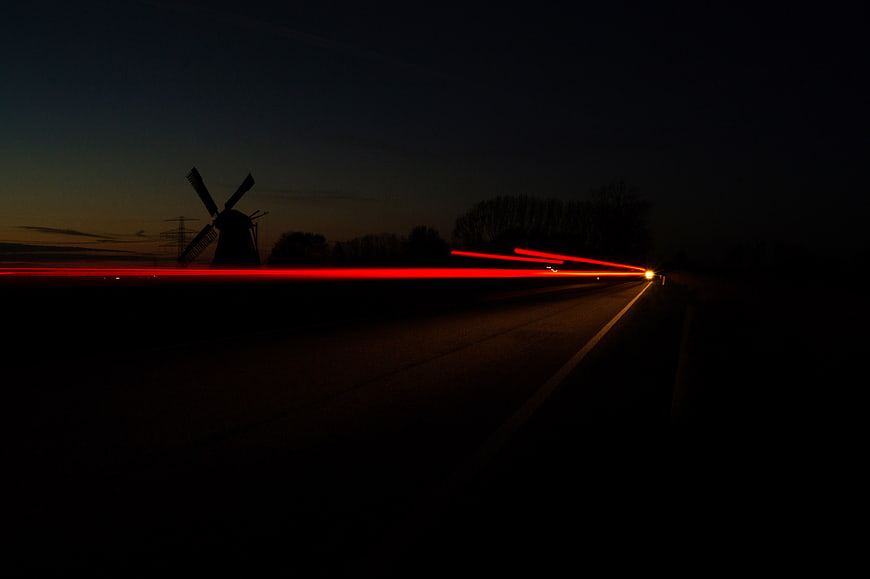 Long exposure red light trails on dark road with windmill silhouette