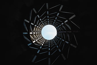 Low angle view of circular metal tunnel structure looking up at sky
