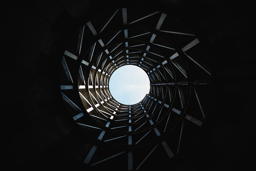 Low angle view of circular metal tunnel structure looking up at sky