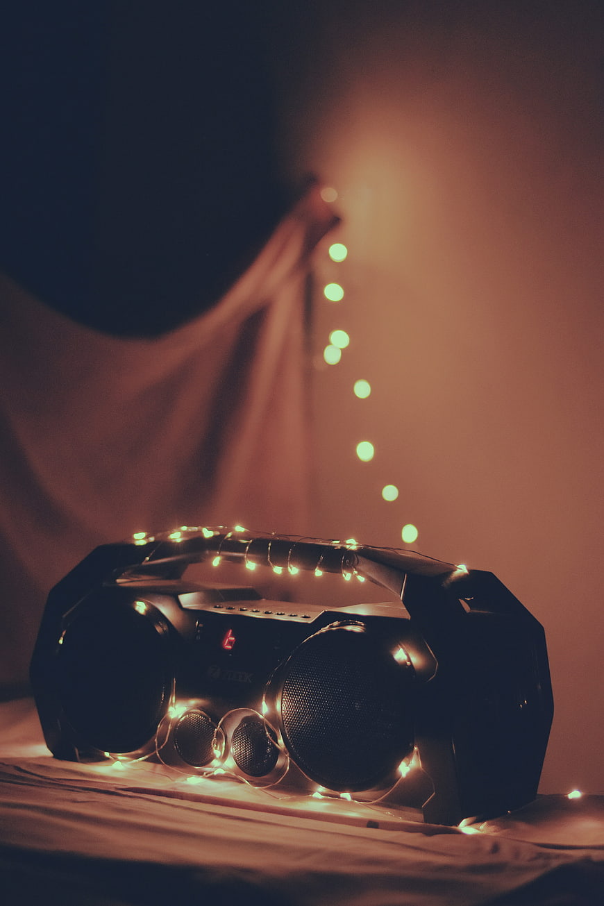 Retro boombox wrapped in fairy lights on a bed