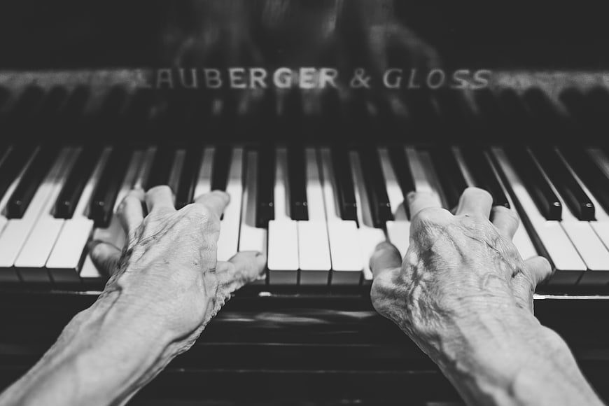 Senior hands playing piano keys in black and white