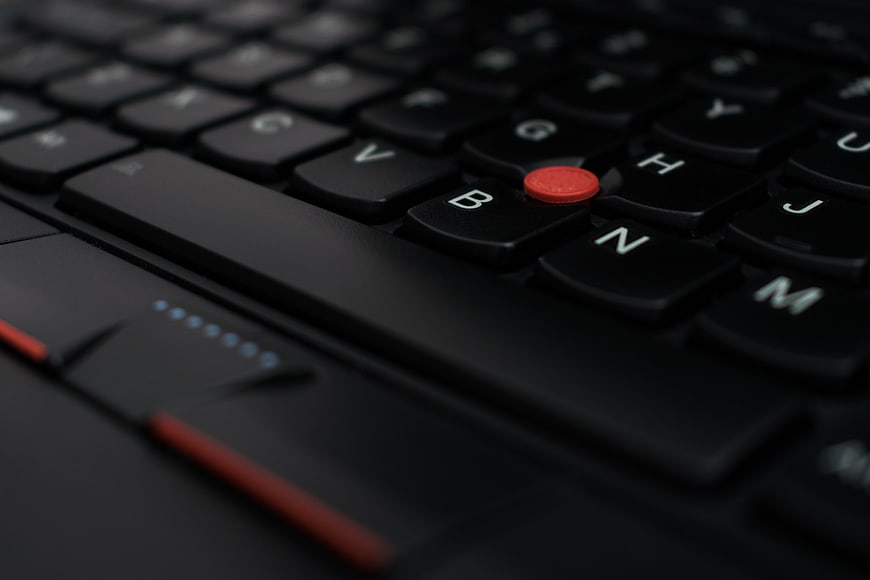 Close-up of a black laptop keyboard with a red trackpoint button
