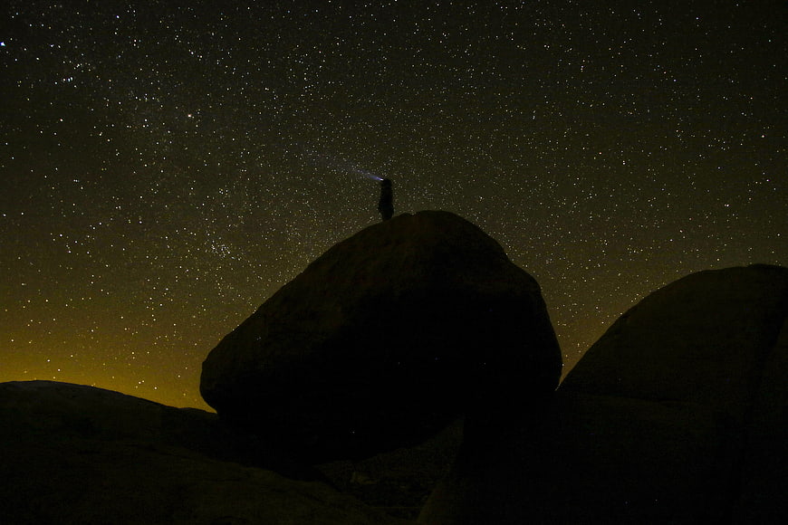Silhouette of person stargazing on rock under Milky Way
