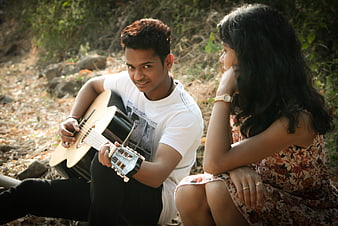 Young Indian couple playing guitar and listening outdoors in nature