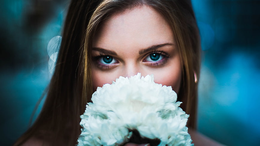 Close-up portrait of woman with blue eyes holding white flower