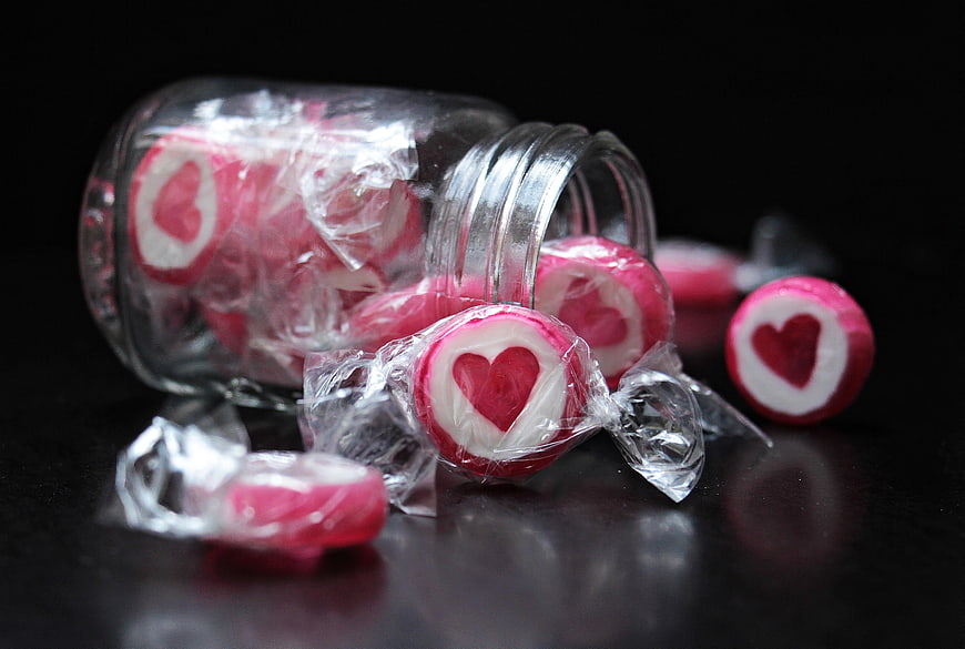 Heart-shaped candies spilling from a glass jar on black background