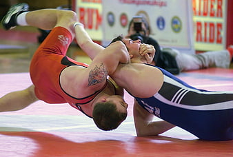 Two male wrestlers grappling intensely on a red competition mat