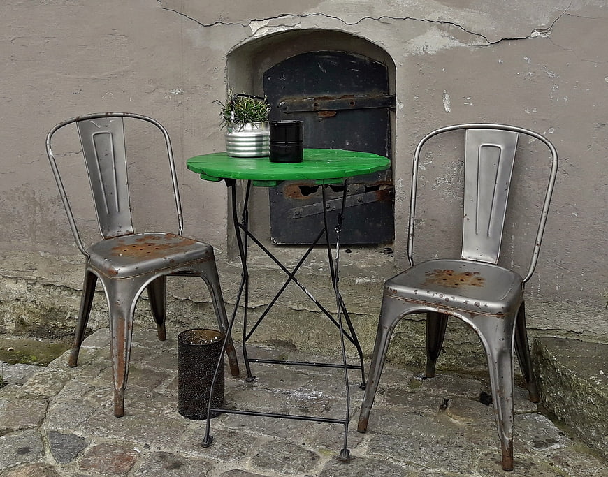 Rusty metal chairs and green table against old stone wall