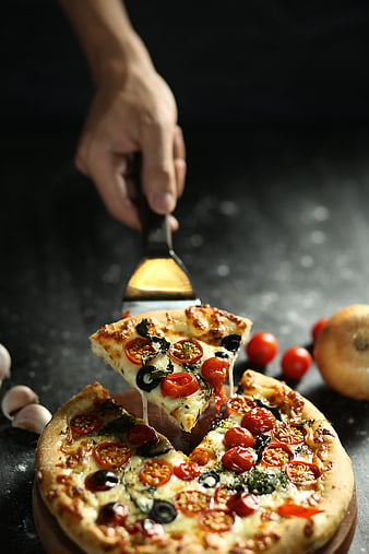 Hand lifting slice of fresh vegetable pizza with melted cheese