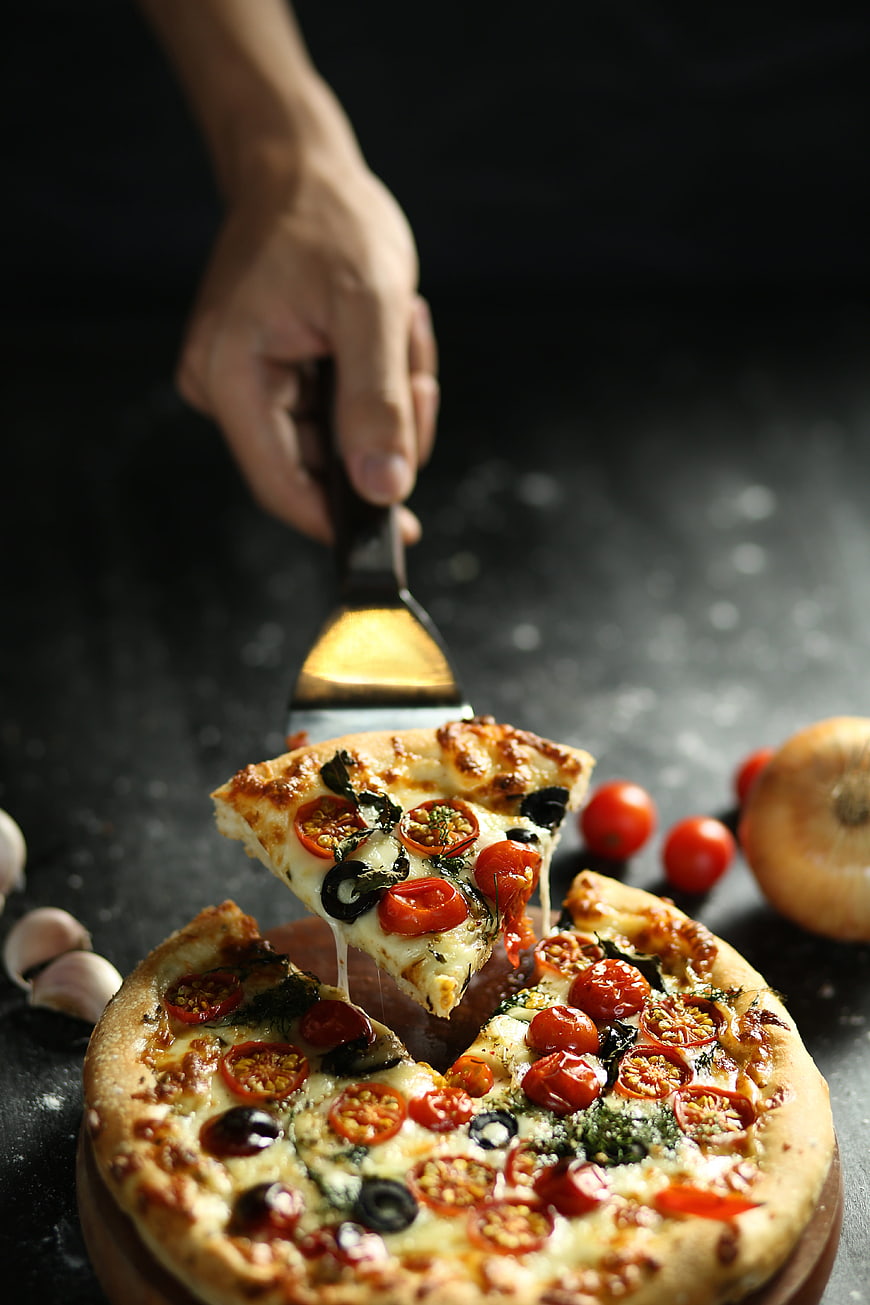 Hand lifting slice of fresh vegetable pizza with melted cheese