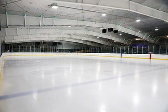 Empty indoor ice hockey rink with white ceiling and boards
