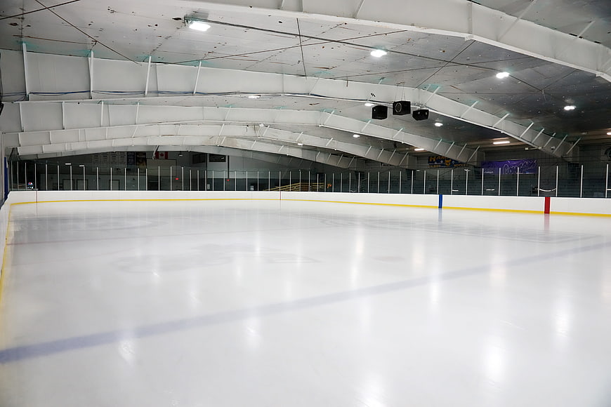 Empty indoor ice hockey rink with white ceiling and boards