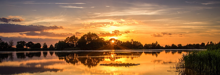 Panoramic sunset over calm lake with tree reflections
