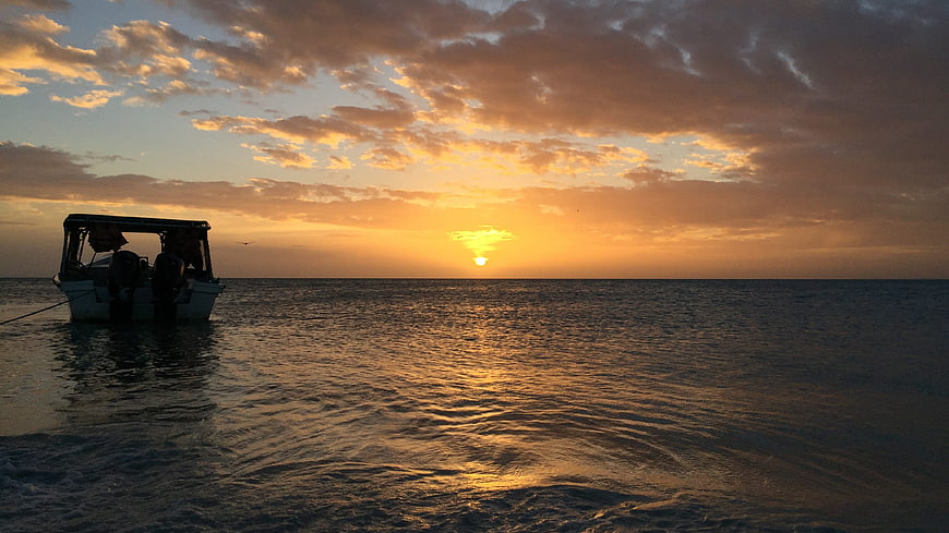 Silhouette of boat on calm ocean during golden sunset