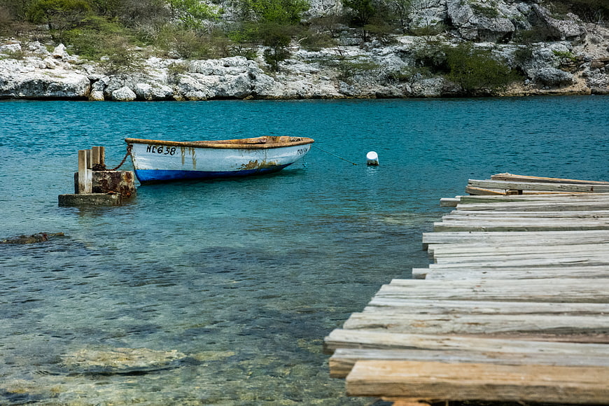 Rustic wooden boat moored near weathered dock in turquoise water