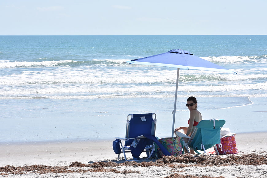 Woman relaxing under blue umbrella on sunny beach