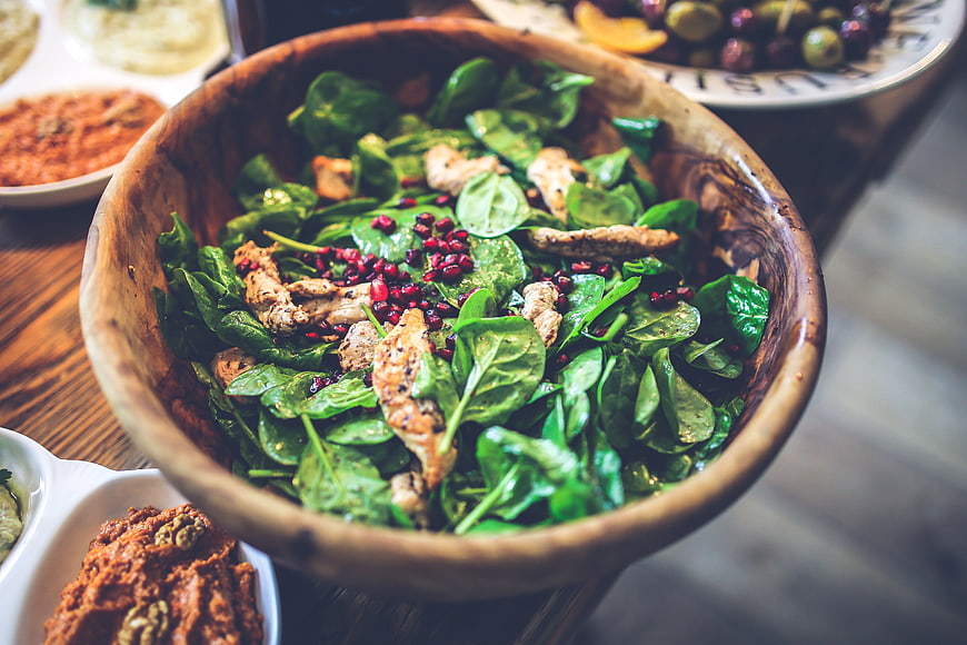 Healthy spinach salad with chicken and pomegranate in a rustic wooden bowl