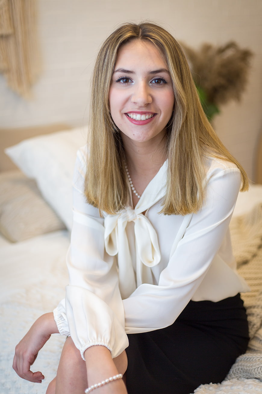 Smiling blonde woman in white blouse sitting on bed