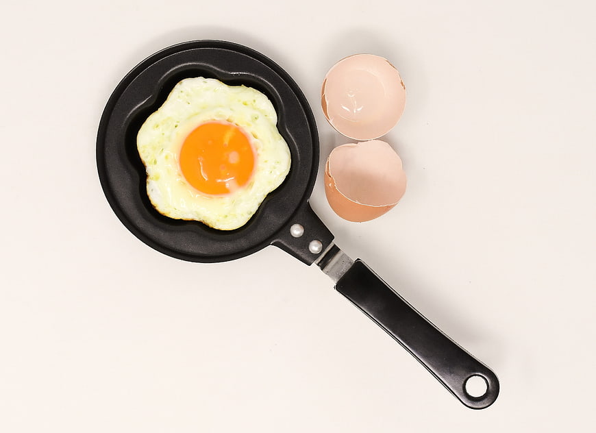 Fried egg in flower-shaped pan with eggshells on white background