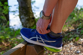 Runner tying blue running shoe on wooden bench outdoors
