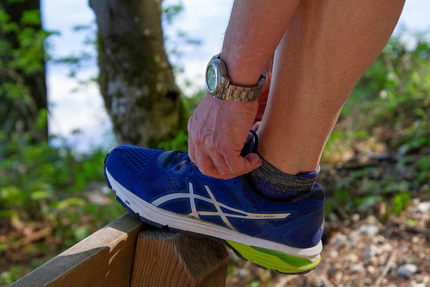 Runner tying blue running shoe on wooden bench outdoors