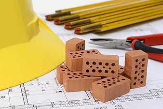 Construction bricks, hard hat, and tools on architectural blueprints