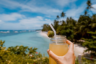 Hand holding tropical drink with ocean beach background