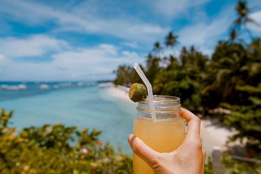 Hand holding tropical drink with ocean beach background