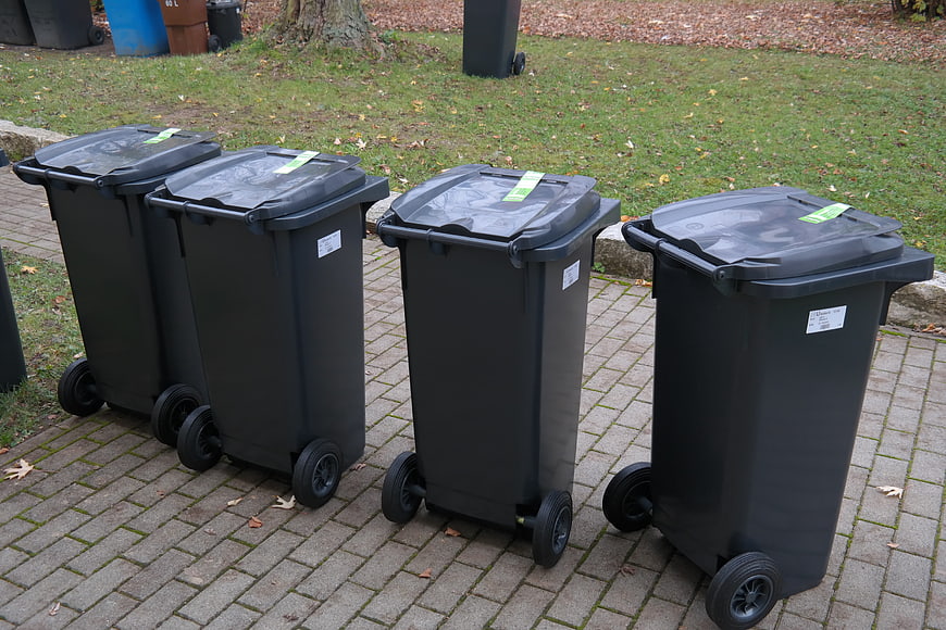 Row of black waste bins on paved sidewalk