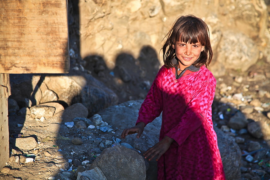 Smiling young girl in pink dress standing in rocky outdoor environment