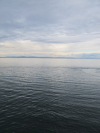 Calm Ocean View with Distant Mountains and Cloudy Sky