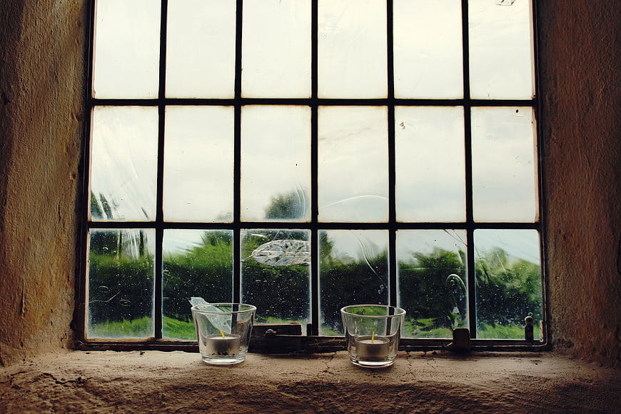 Two tea light candles in glass holders on a rustic stone windowsill