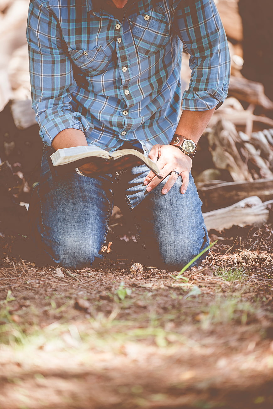 Man kneeling in forest reading book outdoors