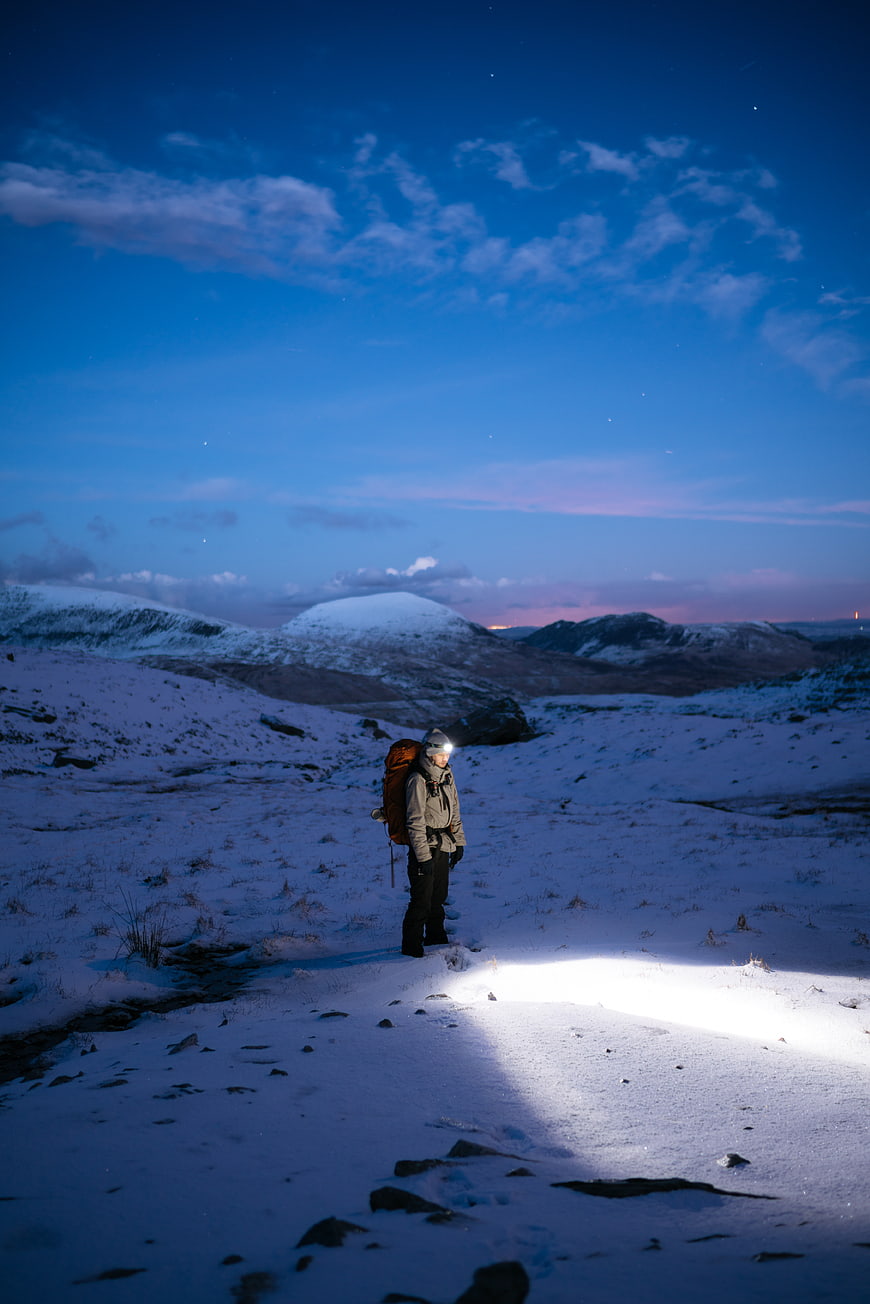 Lone Hiker with Headlamp in Snowy Mountain Landscape at Night