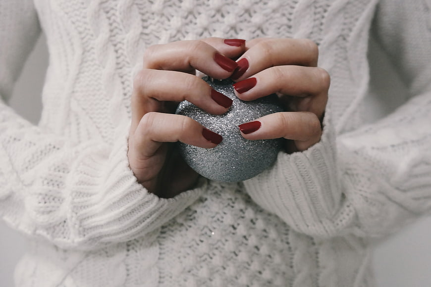 Woman Holding Silver Christmas Ornament in White Sweater
