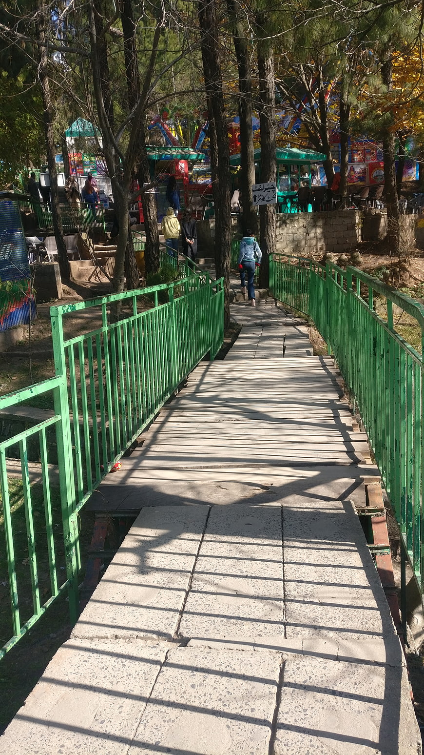 Green metal bridge in park with people walking