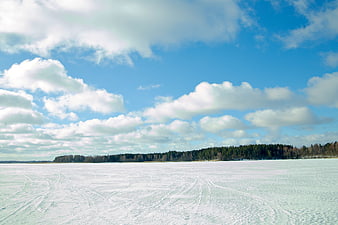 Wide frozen lake landscape with snow tracks and blue sky