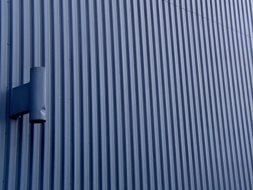 Blue corrugated metal wall with industrial vent pipe