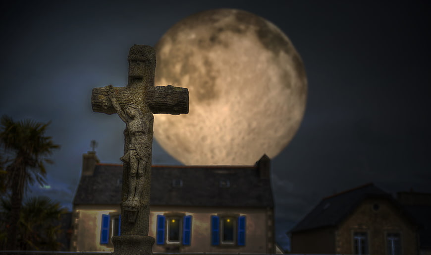 Stone Crucifix Silhouette Against Giant Full Moon at Night