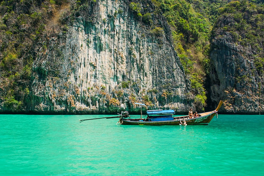 Longtail Boat in Turquoise Waters Near Limestone Cliff
