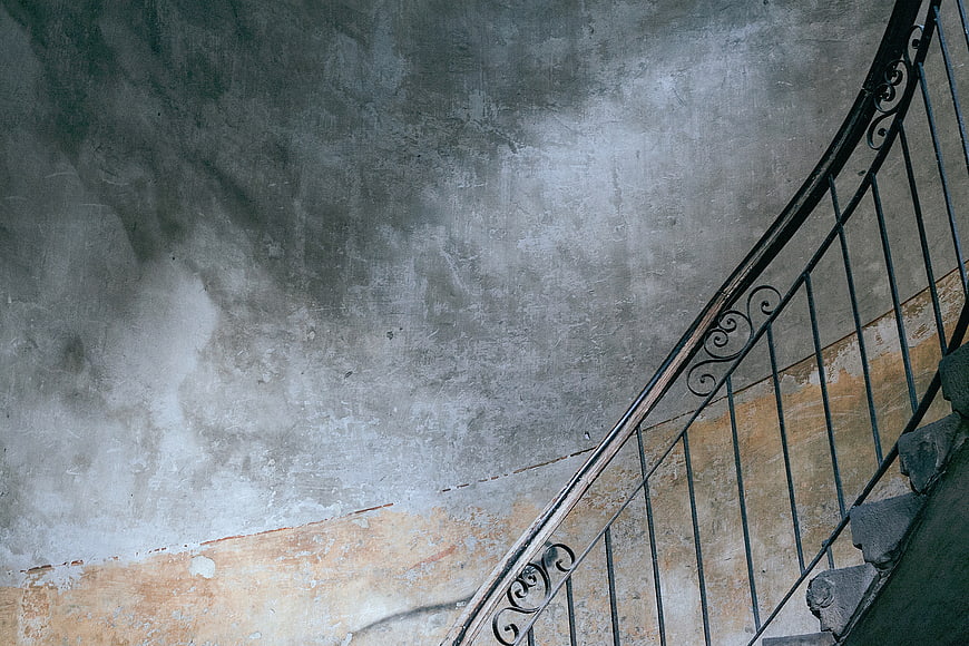 Vintage spiral staircase with wrought iron railing against textured wall