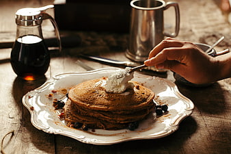 Stack of chocolate pancakes with whipped cream and blueberries on rustic wooden table