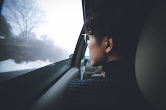 Man with glasses looking out car window at snowy landscape