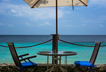 Beachside patio table with chairs and umbrella overlooking turquoise ocean