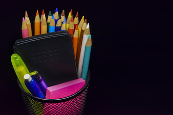 Colorful pencils and stationery in a mesh cup on black background