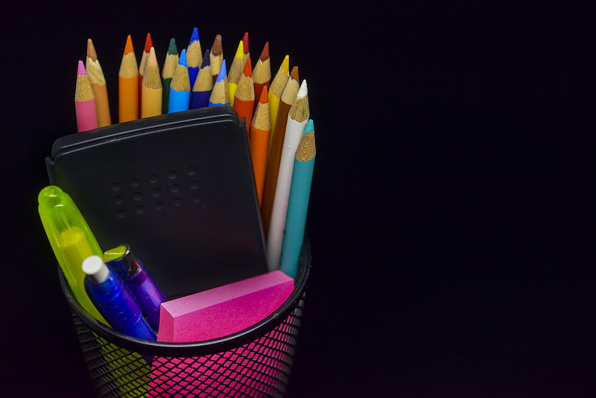 Colorful pencils and stationery in a mesh cup on black background