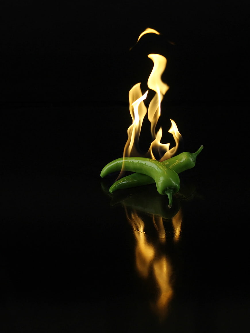 Green chili peppers with flames on black background