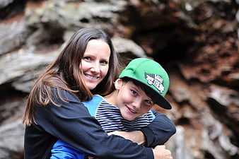 Smiling Mother Hugging Young Boy In Green Cap Outdoors