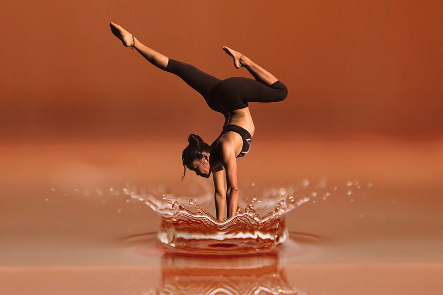 Woman performing handstand in water splash with warm background