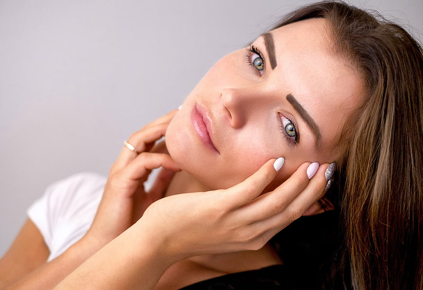Close-up portrait of beautiful woman with blue eyes and hands on face